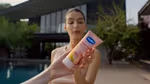 Seorang wanita memegang tabung lotion Vaseline Gluta-Hya berwarna merah muda di luar ruangan.