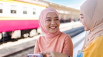 Dua wanita tersenyum di stasiun kereta api.