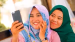 Dua wanita berhijab tersenyum sambil berfoto selfie.